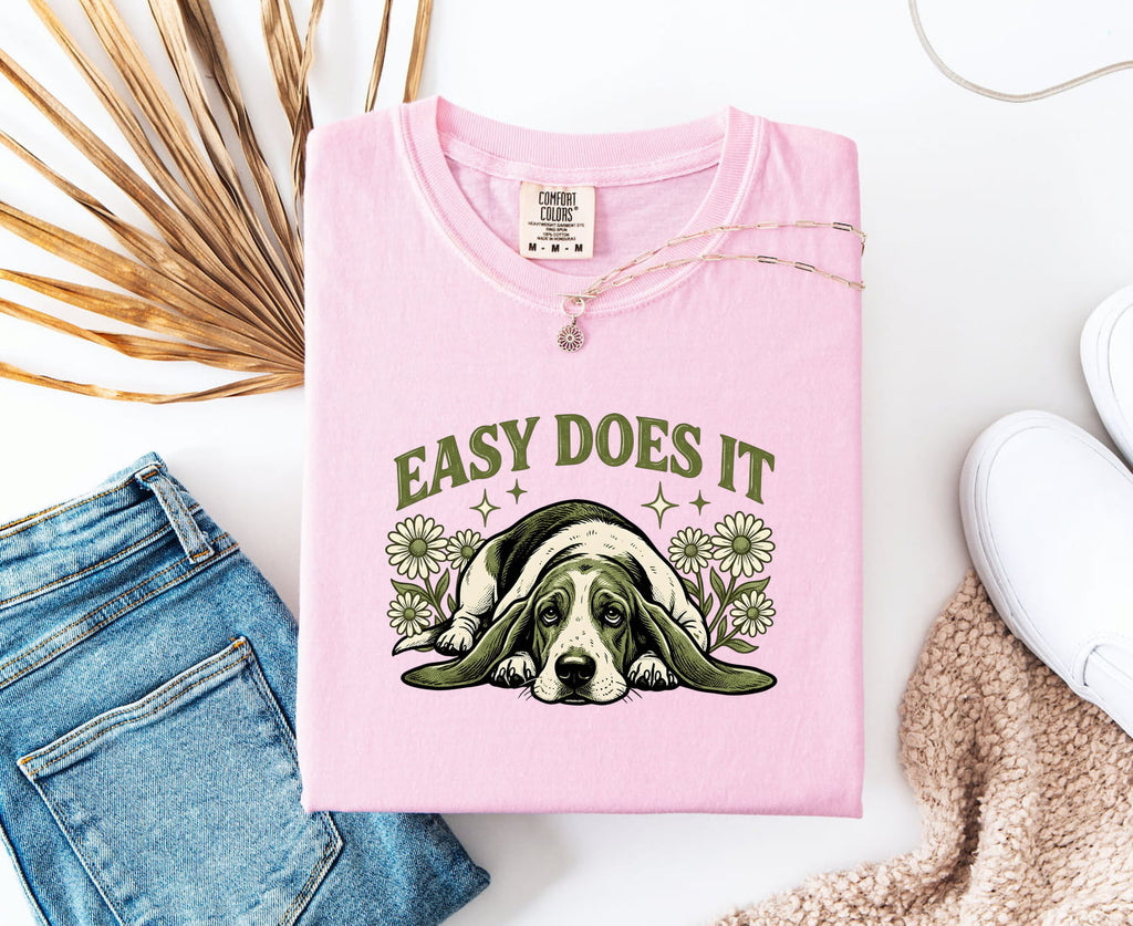 Blossom colored Comfort Colors 1717 t-shirt with a lazy dog graphic and 'Easy Does It' text, folded with jeans and a shoe.