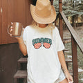 Woman wearing a white Comfort Colors 1717 t-shirt with 'Summer' and sunglasses design, holding a mug on stairs