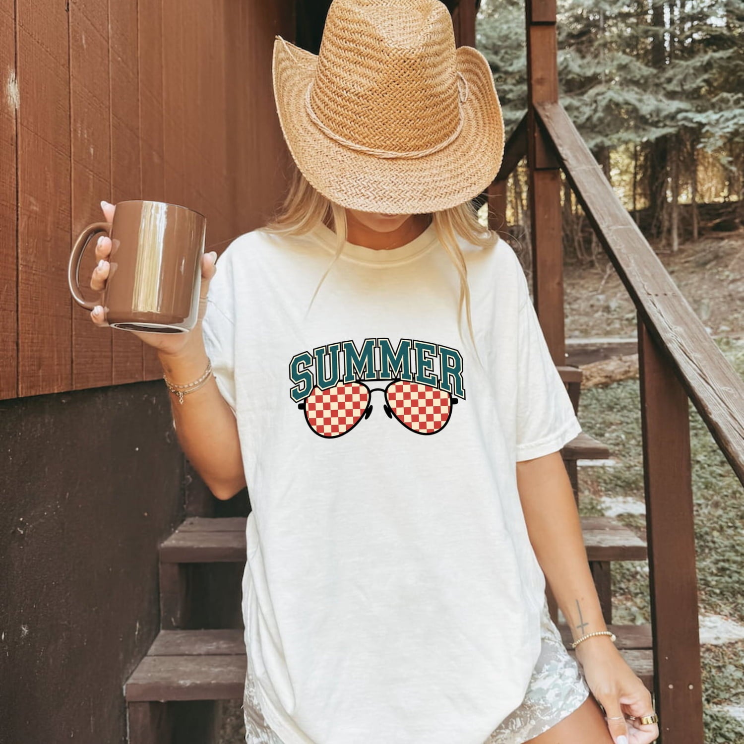 Woman wearing a white Comfort Colors 1717 t-shirt with 'Summer' and sunglasses design, holding a mug on stairs