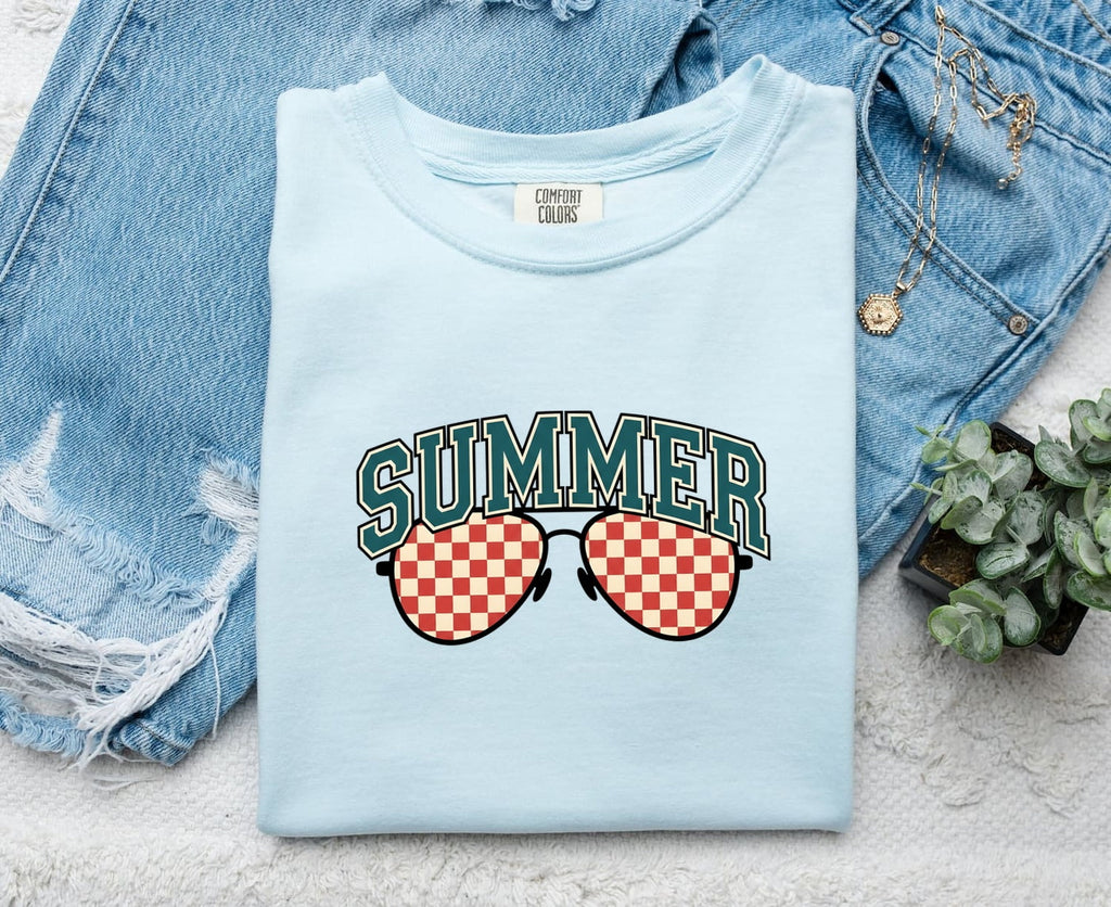 Chambray Comfort Colors 1717 t-shirt with 'Summer' and sunglasses graphic folded on a denim jacket and plant background