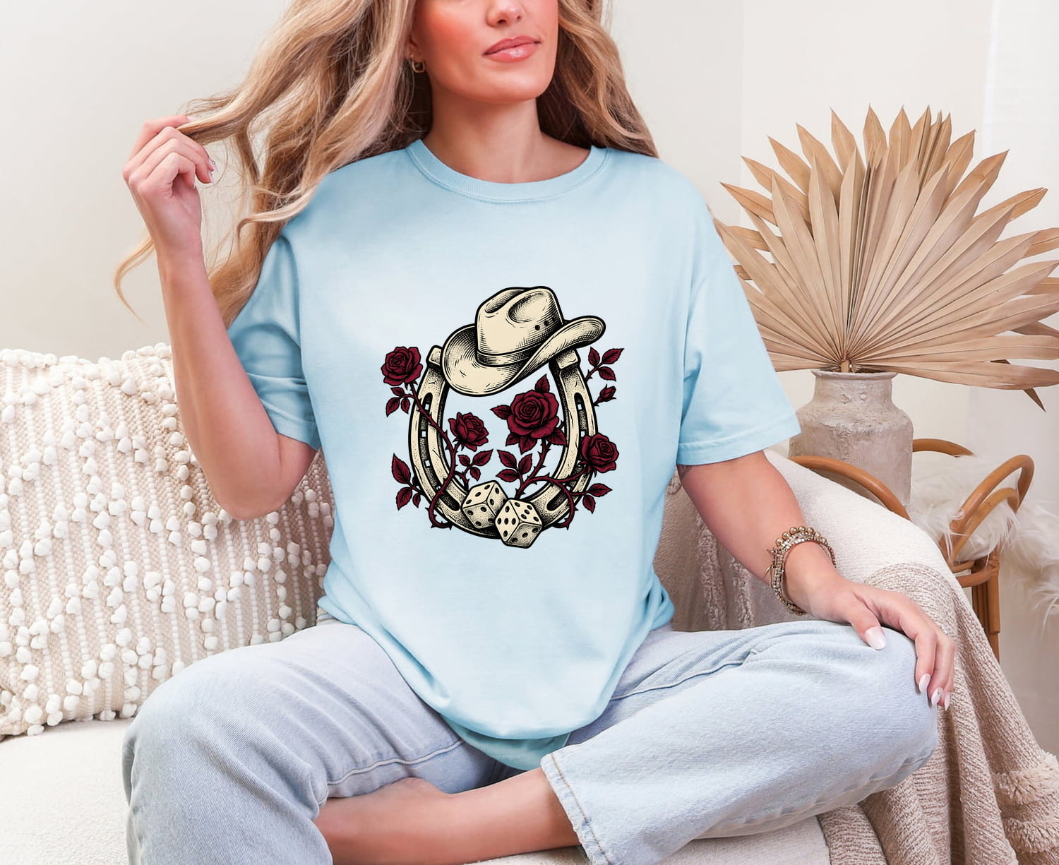 Woman wearing a chambray Comfort Colors 1717 t-shirt with a horseshoe, roses and cowboy hat design, sitting on a couch.