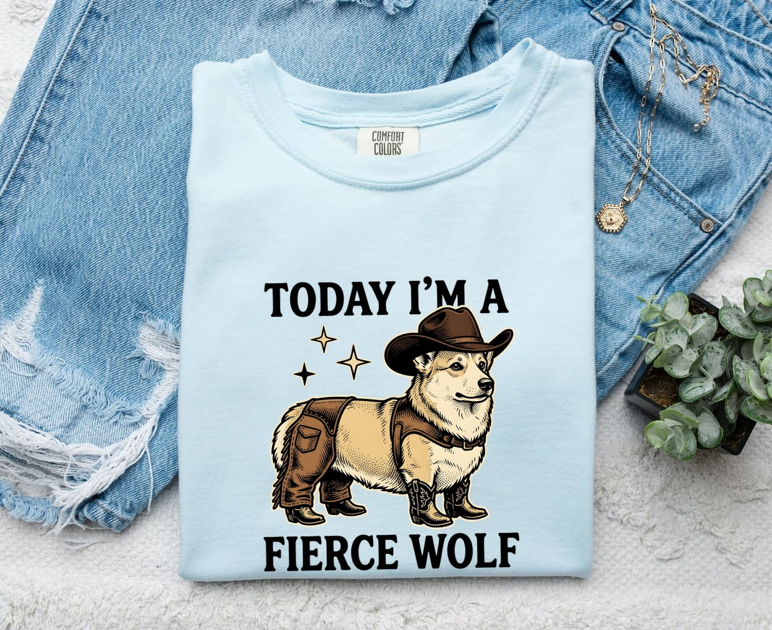 Chambray Comfort Colors 1717 t-shirt with a graphic of a corgi wearing a cowboy hat and boots, text 'Today I'm a fierce wolf', displayed with denim jacket and plant.