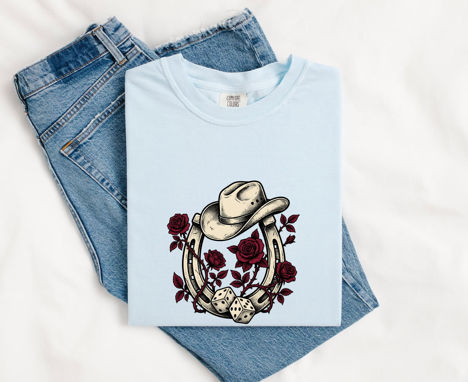 Chambray Comfort Colors 1717 t-shirt with cowboy hat, roses and horseshoe design, folded on jeans
