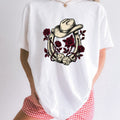 Woman wearing a white Comfort Colors 1717 t-shirt with a cowboy hat, horseshoe, roses, and dice design standing in front of a white background.