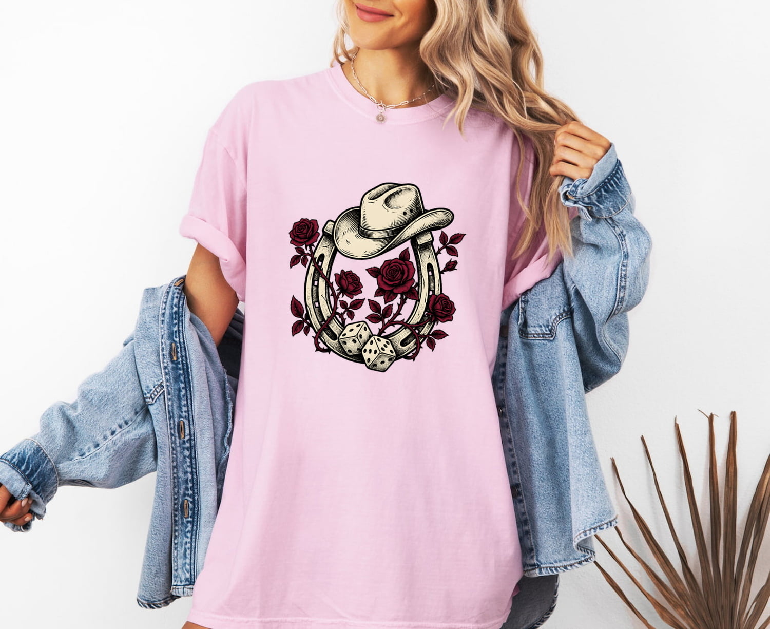 Woman wearing a blossom Comfort Colors 1717 t-shirt with a horseshoe and cowboy hat design, and a denim jacket.