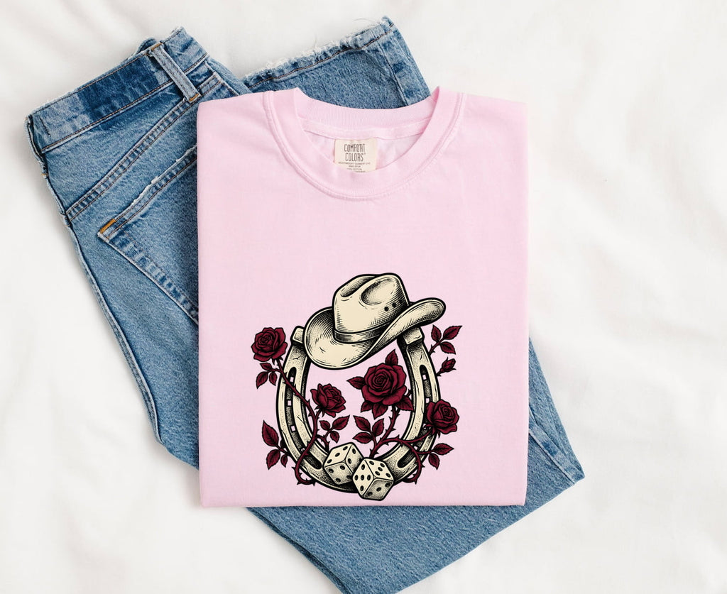 Blossom colored Comfort Colors 1717 t-shirt with horseshoe, roses and cowboy hat graphic, folded on blue jeans