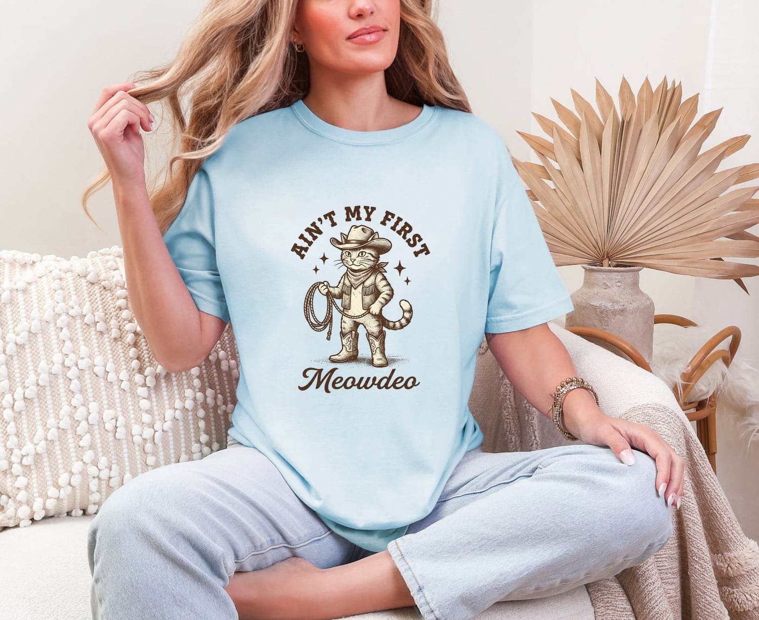Woman wearing a Chambray Comfort Colors 1717 t-shirt with a cat graphic and text, sitting on a couch.