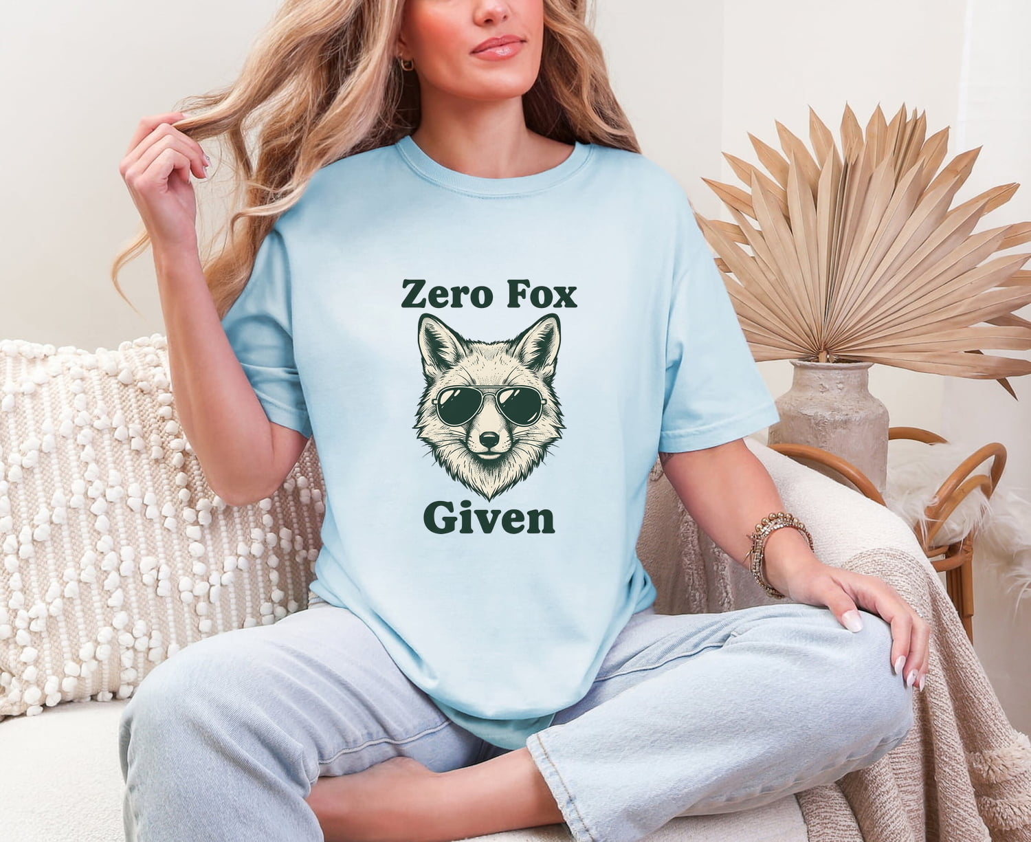 Woman wearing a chambray Comfort Colors 1717 t-shirt with a fox graphic and 'zero fox given' text, sitting on a couch.
