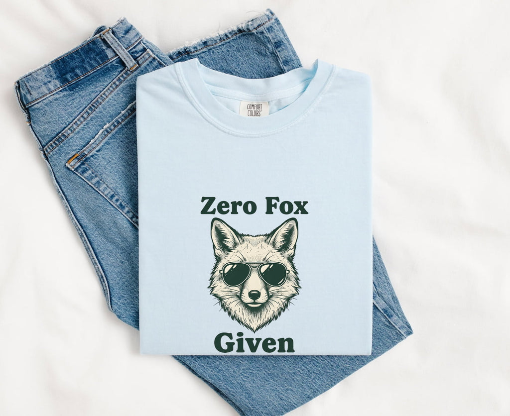 Chambray Comfort Colors 1717 t-shirt with a fox graphic and text, folded with jeans on a white background