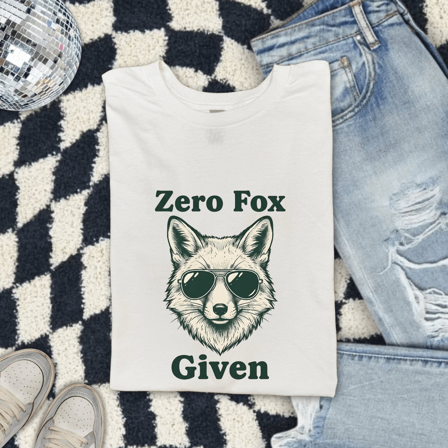 White Comfort Colors 1717 t-shirt with a fox graphic and text 'Zero Fox Given' on a checkered rug with jeans and shoes.