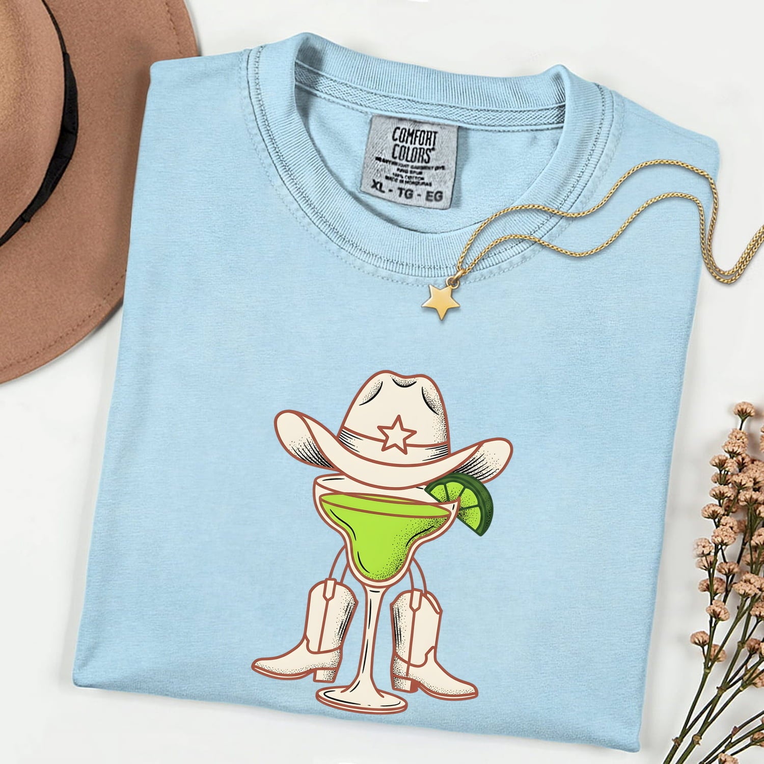 Chambray colored Comfort Colors 1717 t-shirt with a cartoon design of a cocktail wearing a cowboy hat and boots, on a white background.