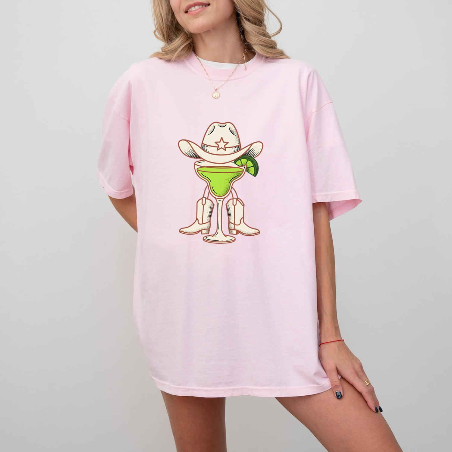 Woman wearing a Blossom Comfort Colors 1717 t-shirt with a margarita cowboy and boots graphic design on a plain background
