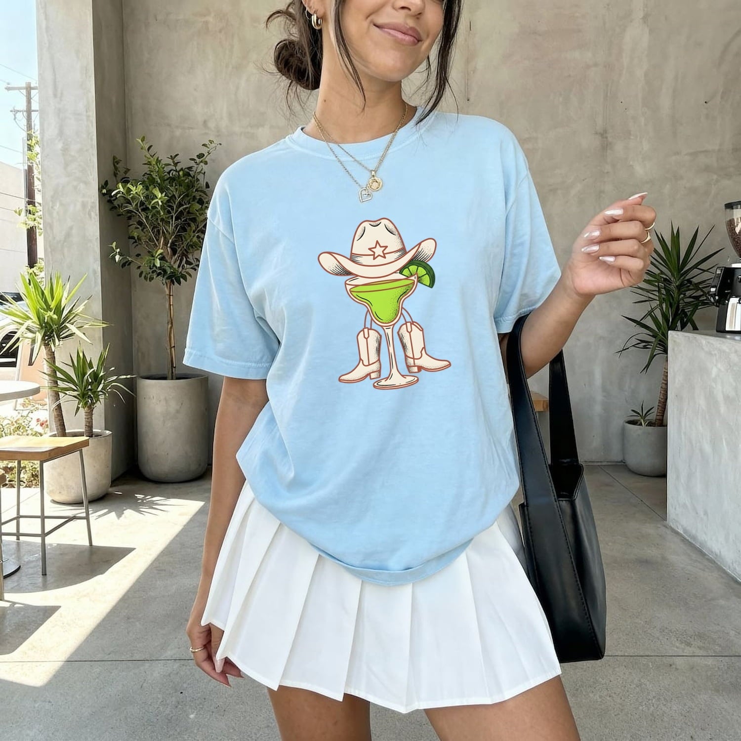 Woman wearing a chambray comfort Colors 1717 t-shirt with a western themed cocktail graphic design in an outdoor setting