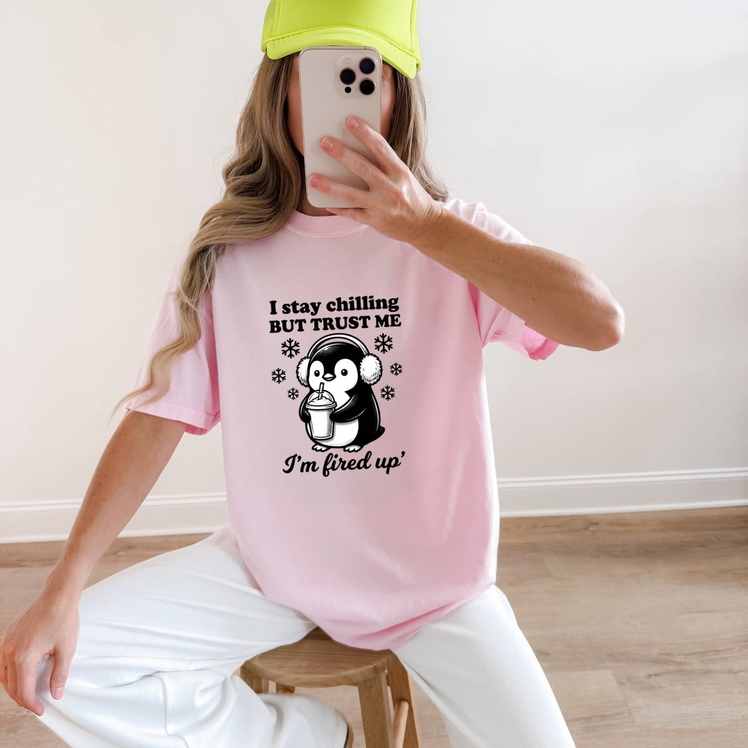 Woman wearing a blossom Comfort Colors 1717 t-shirt with a penguin graphic and funny text, sitting on a wooden stool.