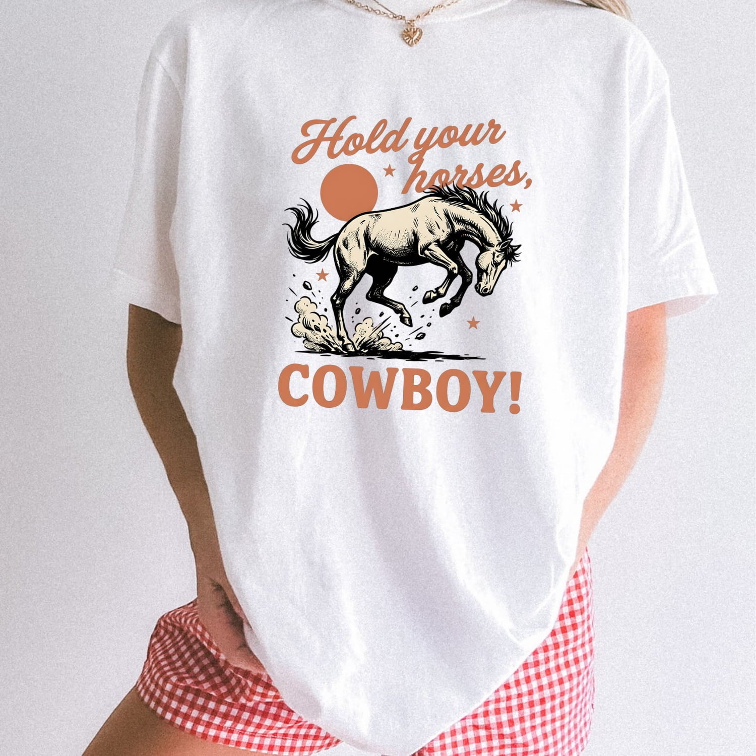 Woman standing wearing a white Comfort Colors 1717 t-shirt with a horse graphic and text 'Hold your horses, cowboy!' on a plain background.