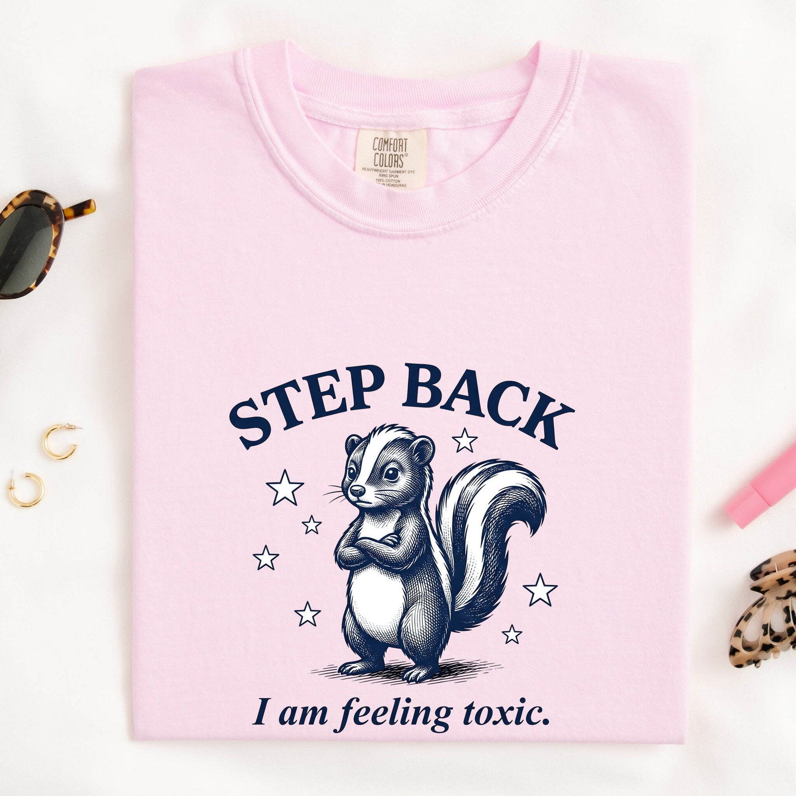 Blossom Comfort Colors 1717 t-shirt with a skunk graphic and 'Step Back' text, folded on a white background