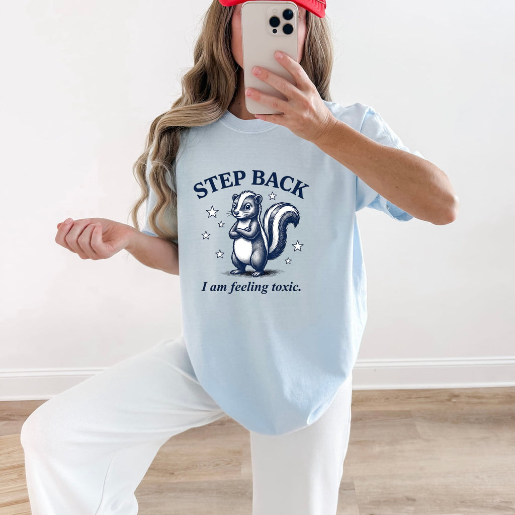 Woman wearing a chambray Comfort Colors 1717 t-shirt with a graphic of a skunk and funny text, taking a mirror selfie.