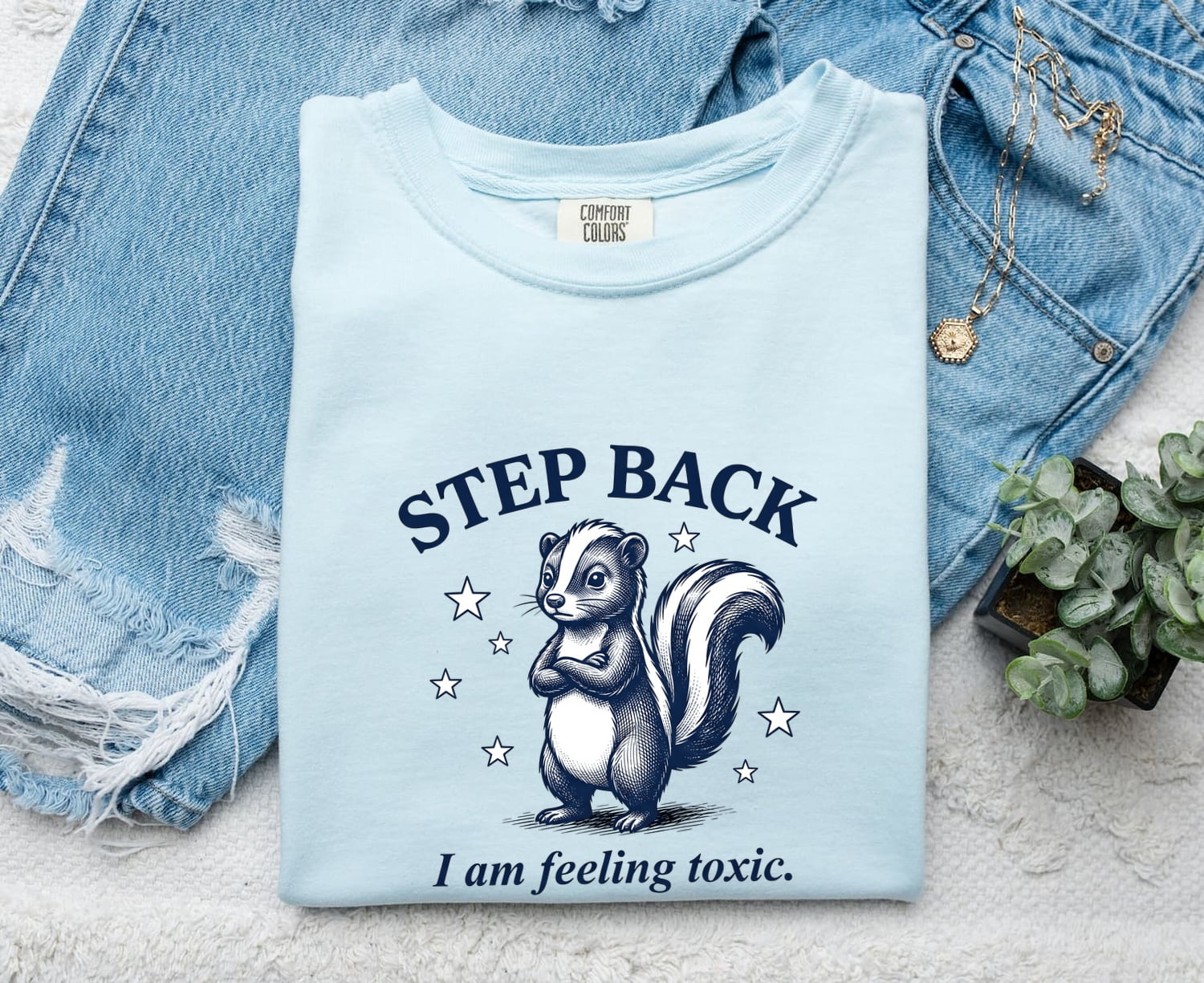 Chambray Comfort Colors 1717 t-shirt with a graphic of a skunk and text 'Step Back I am feeling toxic' on a denim background.