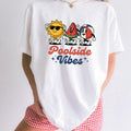 Woman wearing a White Comfort Colors 1717 t-shirt with 'Poolside Vibes' design featuring sun, watermelon, and beach ball against a plain background