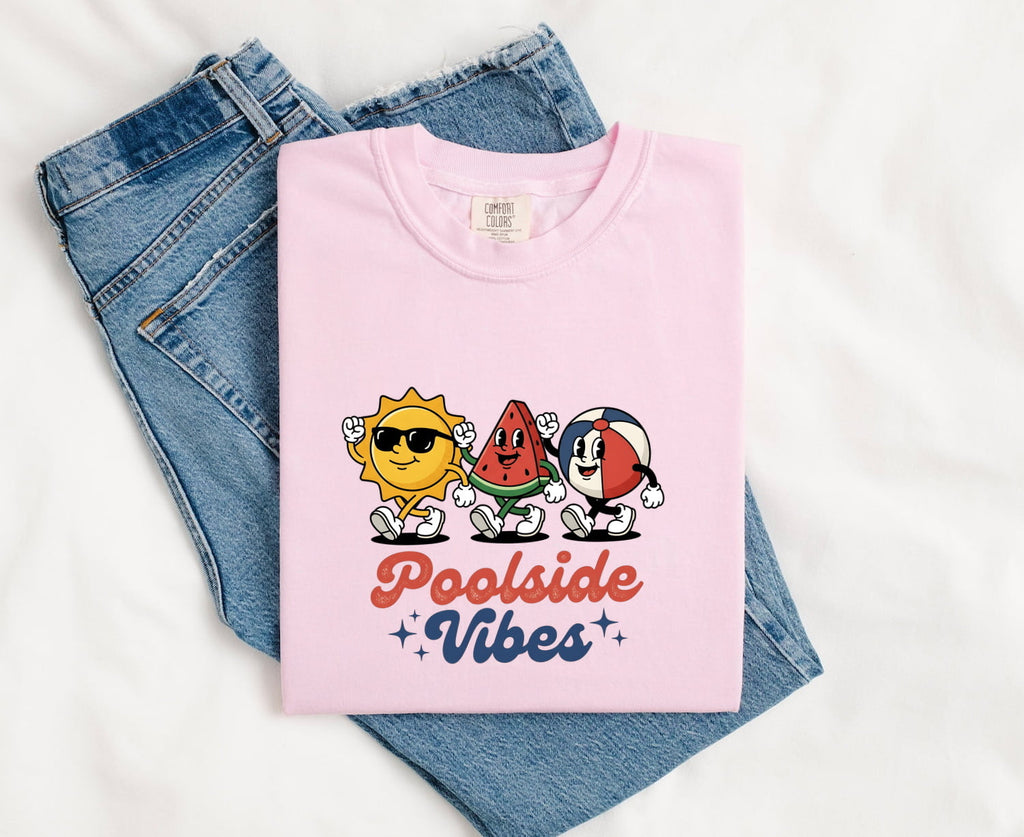 Blossom Comfort Colors 1717 t-shirt with 'Poolside Vibes' text and cartoonish characters, folded on blue jeans