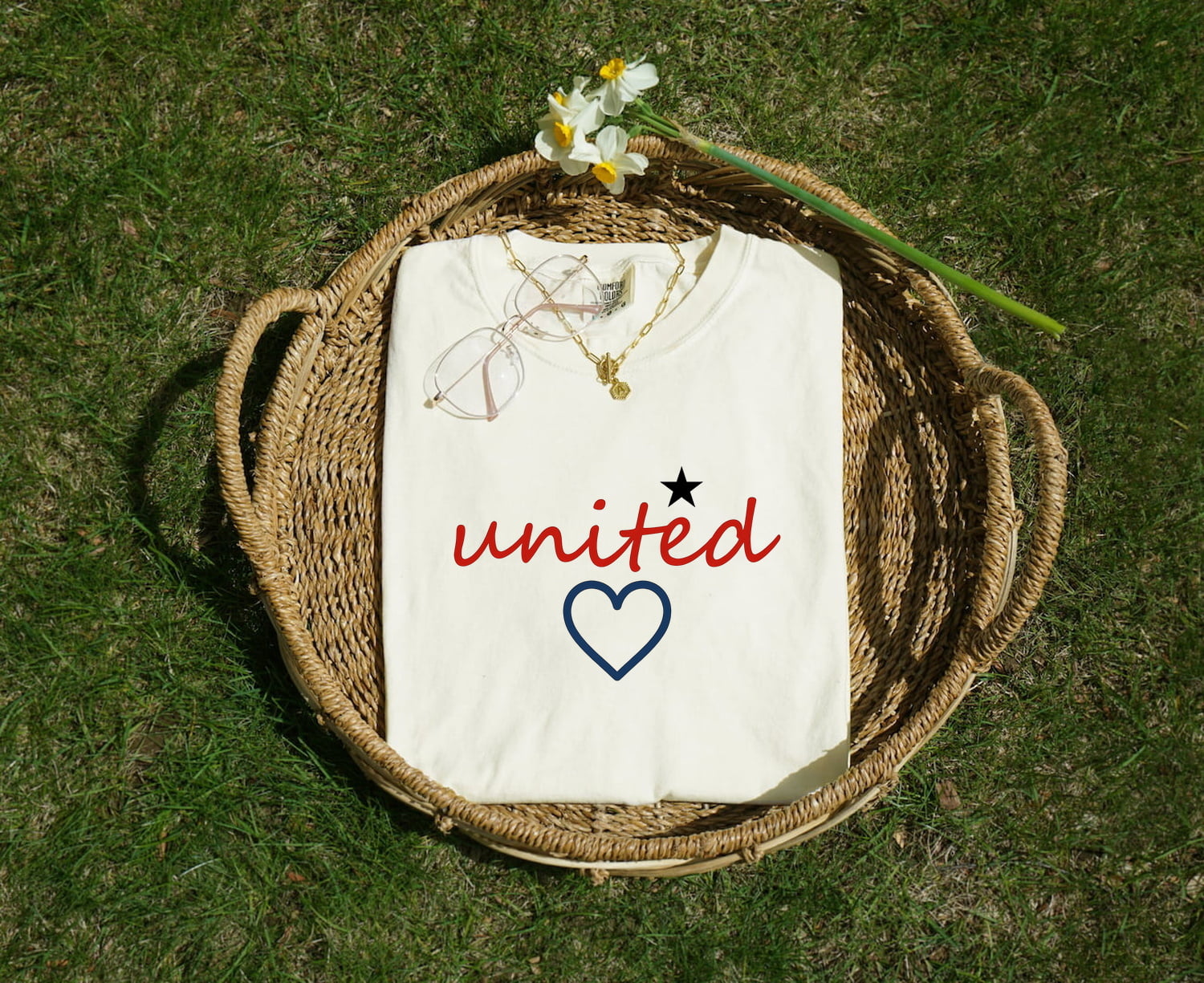 White Comfort Colors 1717 t-shirt with 'united' design, folded in a woven basket on grass