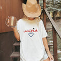 Woman wearing a white Comfort Colors 1717 t-shirt with 'united' design, holding a mug on a wooden stairway.