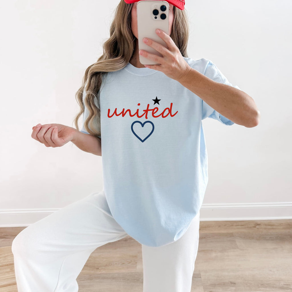 Woman wearing a Chambray Comfort Colors 1717 t-shirt with 'united' and a heart design, taking a mirror selfie.