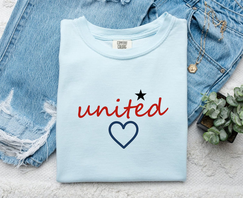 Chambray Comfort Colors 1717 t-shirt with 'united' text and heart design, folded on a denim background.