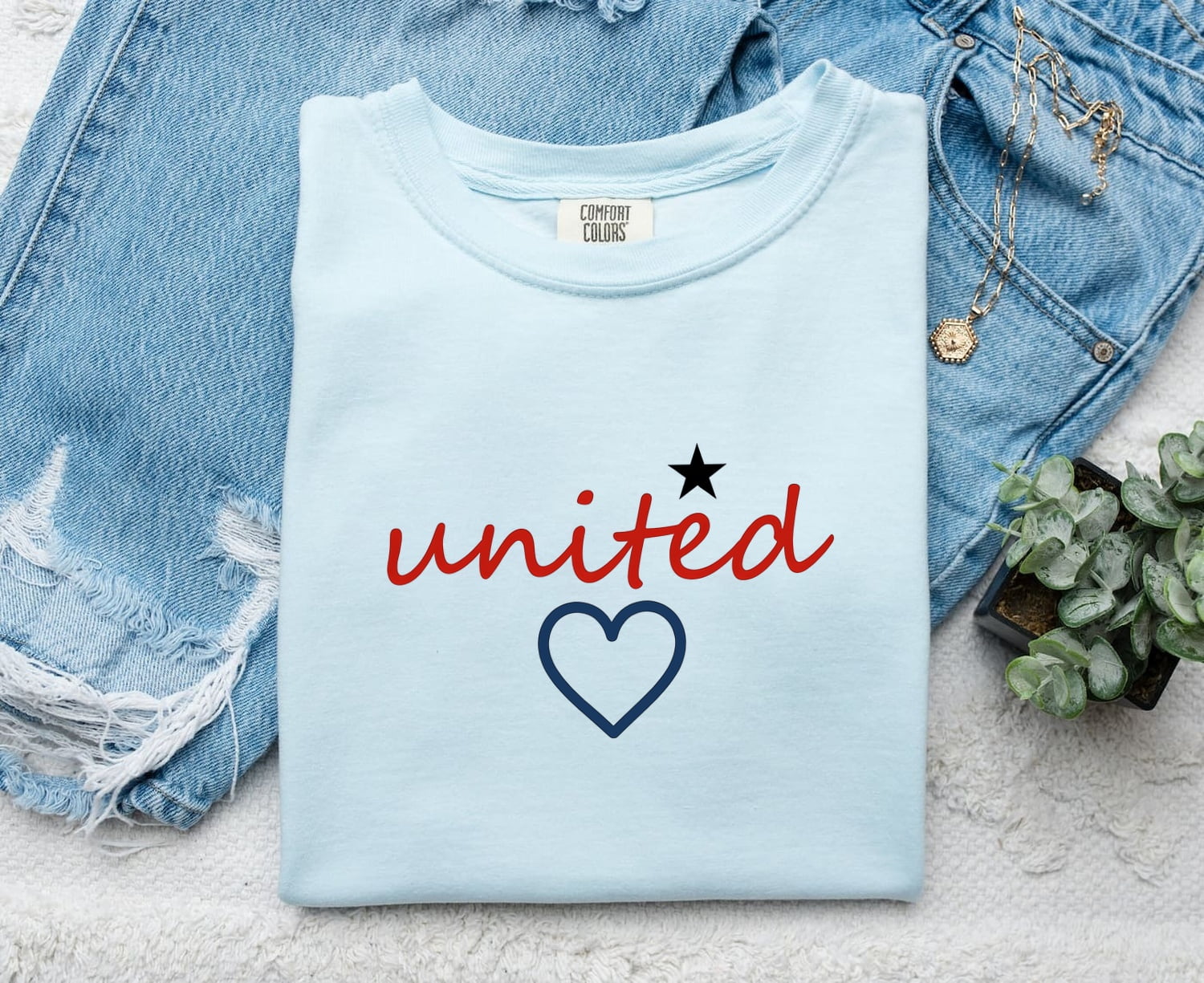 Chambray Comfort Colors 1717 t-shirt with 'united' text and heart design, folded on a denim background.